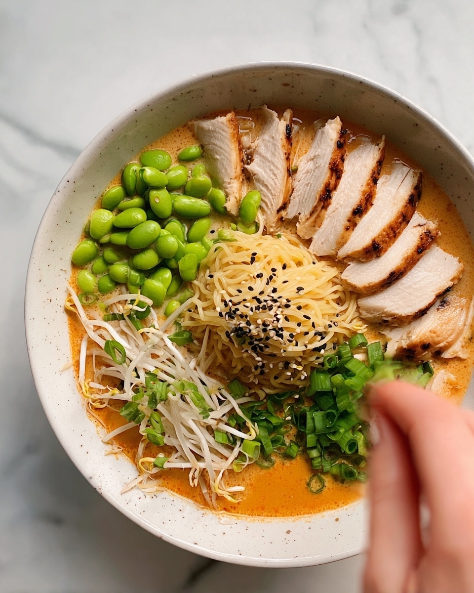 A white bowl with a soup base in orange color fills the bottom. On top, in clockwise order from the top right, are six slices of cooked chicken with a light golden crust and white inside, bright green chopped scallions, a pile of light beige bean sprouts, green edamame beans, and more chopped scallions. In the middle is a small mound of creamy yellow noodles, slightly shiny from the soup, with black sesame seeds sprinkled over the chicken, noodles, and scallions. A woman's hand is placing bean sprouts into the bowl, slightly blurred, with a white marbled surface under the bowl photo taken with an iphone --ar 4:5 --v 7