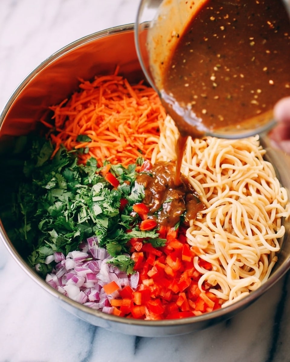 A shiny mixing bowl filled with five distinct layers: pale beige cooked noodles at the bottom right, finely chopped bright red bell peppers next to the noodles, shredded orange carrots layered beside the bell peppers, finely chopped light purple onions on the edge near the carrots, and fresh green cilantro filling the bowl's upper edge. A thick brown sauce with visible bits is being poured from a clear measuring cup into the center of the bowl. The bowl sits on a white marbled surface, and a woman's hand holds the measuring cup. photo taken with an iphone --ar 4:5 --v 7