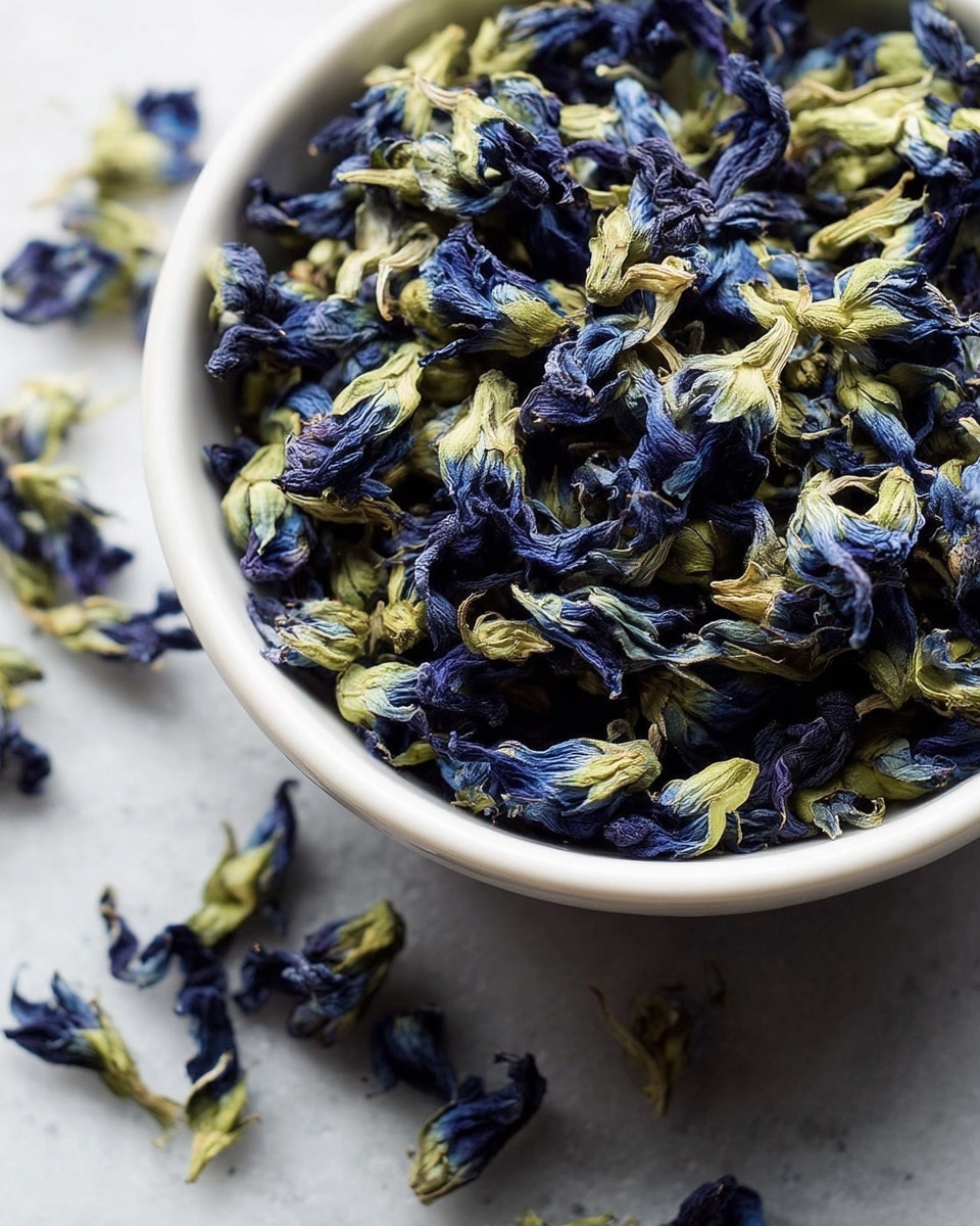 A white bowl filled with a pile of dried blue and green flowers with slightly wrinkled petals and stems, some flowers spilled outside the bowl onto a white marbled surface, the blue parts showing deep navy shades blending into light greenish-yellow on the stems, creating a textured and natural look, all tightly packed with a mix of curled and elongated shapes photo taken with an iphone --ar 4:5 --v 7