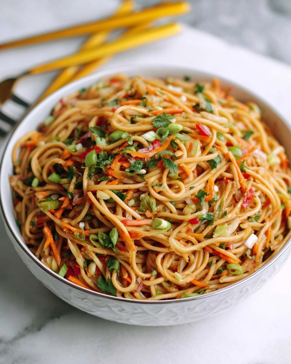 A large white bowl filled with long, light brown noodles mixed with finely chopped vegetables including green onions, red bell peppers, orange carrots, and green herbs scattered throughout. The noodles have a glossy texture and are twisted together in loose layers, with the colorful vegetables evenly distributed on top and within. The bowl sits on a white marbled surface, and in the blurred background, there are yellow-handled utensils resting on the same surface. photo taken with an iphone --ar 4:5 --v 7