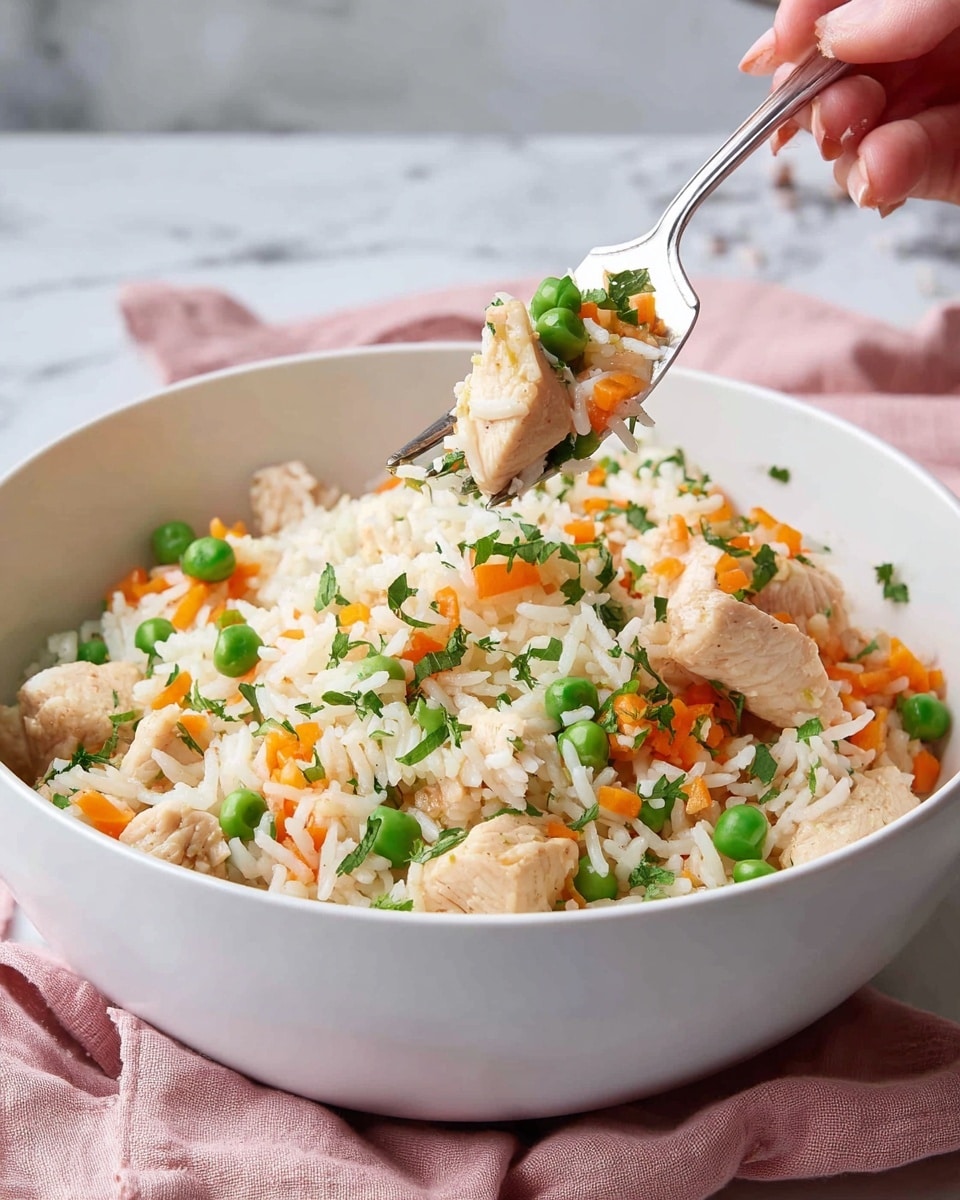 A white bowl holds a mix of fluffy white rice layered with small colorful pieces of orange carrot strips and bright green peas, along with tender, light brown chicken chunks scattered evenly. Fresh chopped green herbs are sprinkled on top, adding a fresh touch. A shiny silver fork with a piece of chicken, rice, one green pea, and carrot is lifted above the bowl by a woman's hand. The bowl sits on a soft pink cloth, all placed on a white marbled surface. Photo taken with an iphone --ar 4:5 --v 7