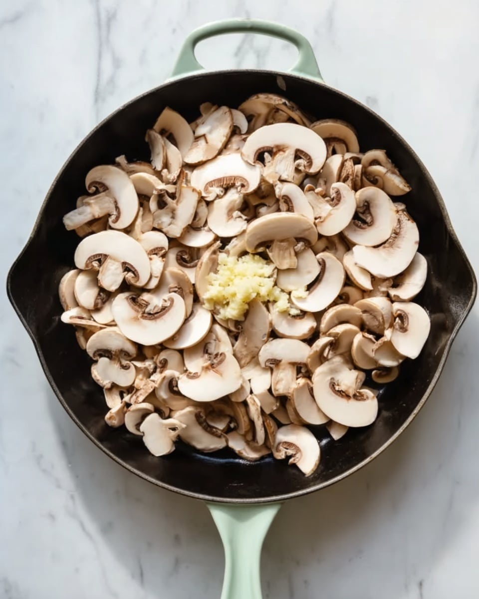 A black cast iron pan with a light green handle sits on a white marbled surface, filled with many slices of fresh mushrooms that are light brown and white with smooth, curved shapes. In the center of the mushrooms, there is a small dollop of pale yellow minced garlic. The mushrooms cover the entire pan, creating a soft, layered texture with gentle shadows on their edges. The photo taken with an iphone --ar 4:5 --v 7