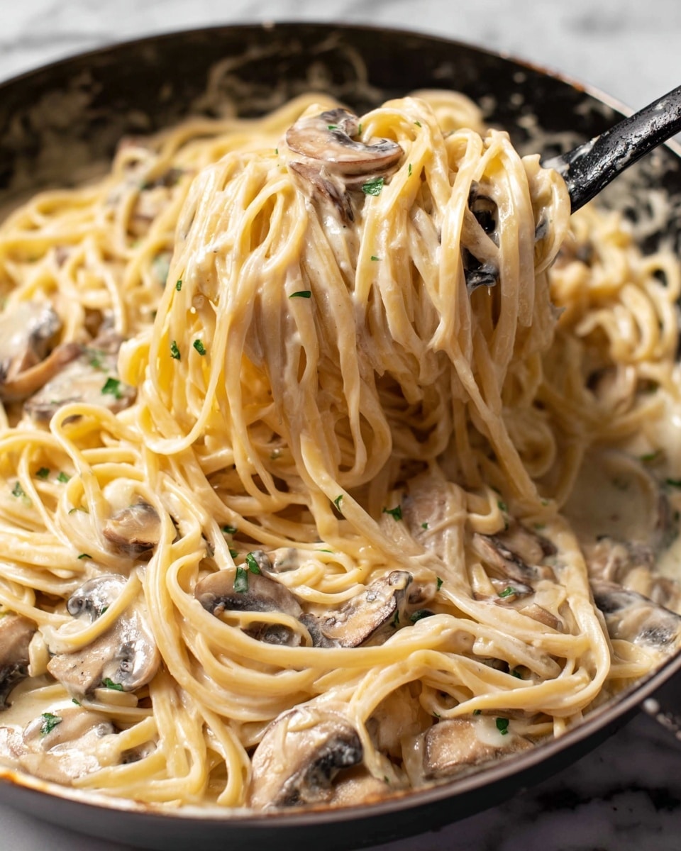 This close-up image shows creamy pasta with mushrooms in a black skillet on a white marbled surface. The pasta strands are long, smooth, and pale yellow, covered in a thick cream sauce that looks rich and glossy. Mixed in the sauce are thin slices of cooked mushrooms, light brown with darker edges, scattered throughout. A black spoon lifts some of the pasta, gently twisting it in the sauce and mushrooms, creating a soft, cloud-like texture with visible small green herbs scattered in the cream. The light reflects softly on the sauce, highlighting its creamy and smooth texture. photo taken with an iphone --ar 4:5 --v 7