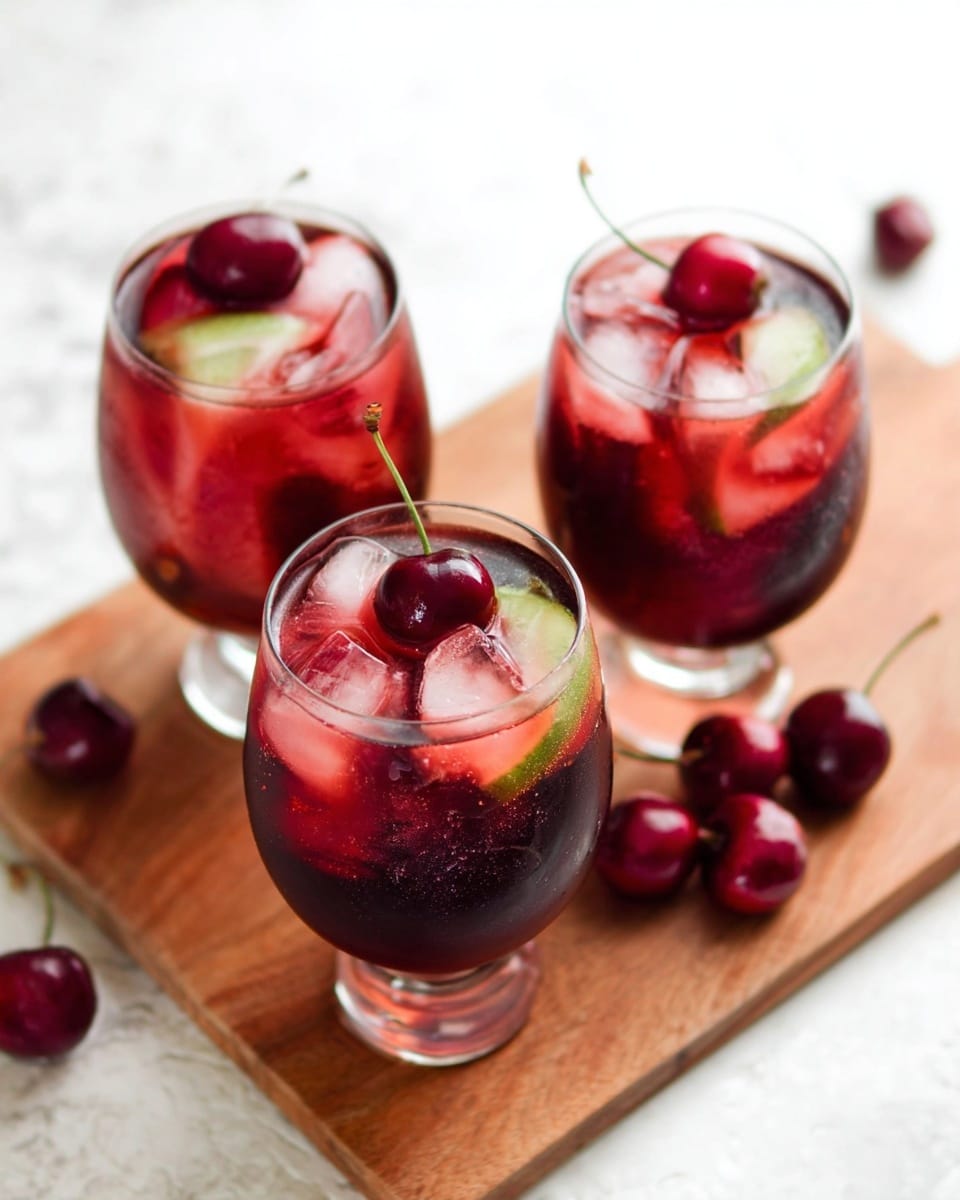 Three glasses filled with a dark red drink, each containing a large ice cube with a pink and green slice inside. Each glass is garnished with a bright red cherry placed on the rim or inside the drink. The glasses stand on a wooden board with a few cherries scattered around it. The background is a clean white marbled texture. photo taken with an iphone --ar 4:5 --v 7