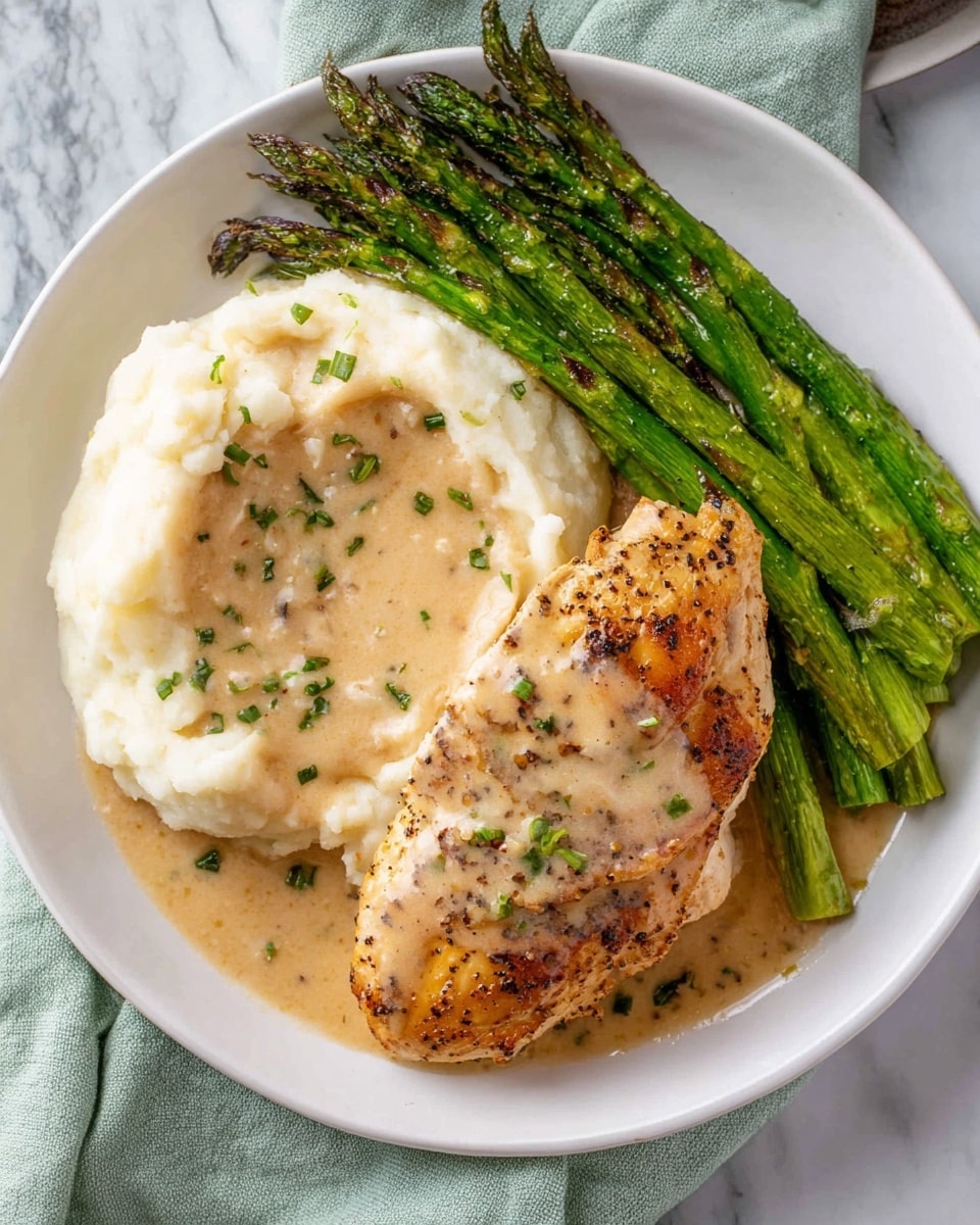 The image shows a white round plate with three main parts: on the left, there is a pile of smooth, creamy white mashed potatoes topped with light beige creamy sauce that has small green herb pieces. On the right side, there is a golden brown cooked chicken piece with black pepper and bits of herbs on top, resting partly on the mashed potatoes and sauce. Above the chicken, there is a bunch of bright green cooked asparagus with some dark grill marks, slightly glossy in texture. The plate sits on a light green cloth on a white marbled surface. Photo taken with an iphone --ar 4:5 --v 7