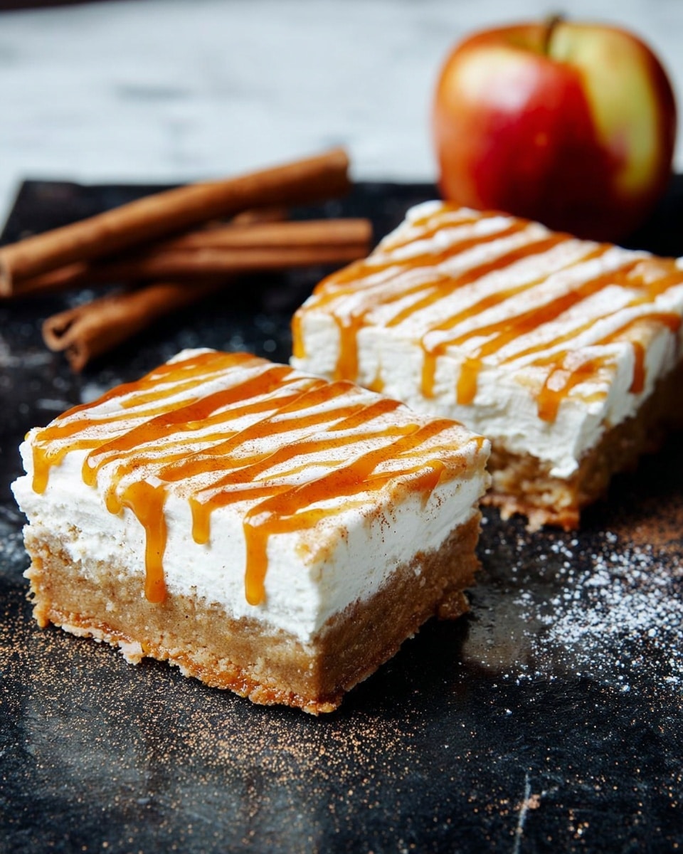 Two square dessert bars sit on a dark surface; each bar has two layers with a thick, light brown base that looks soft and crumbly, topped by a thick white creamy layer that is smooth and fluffy. Orange syrup is drizzled in thin stripes over the white layer, dripping slightly over the edges. Behind the bars, a half apple with a red and yellow skin and two cinnamon sticks lie casually on the surface, adding warm colors. The setting is on a white marbled texture. photo taken with an iphone --ar 4:5 --v 7