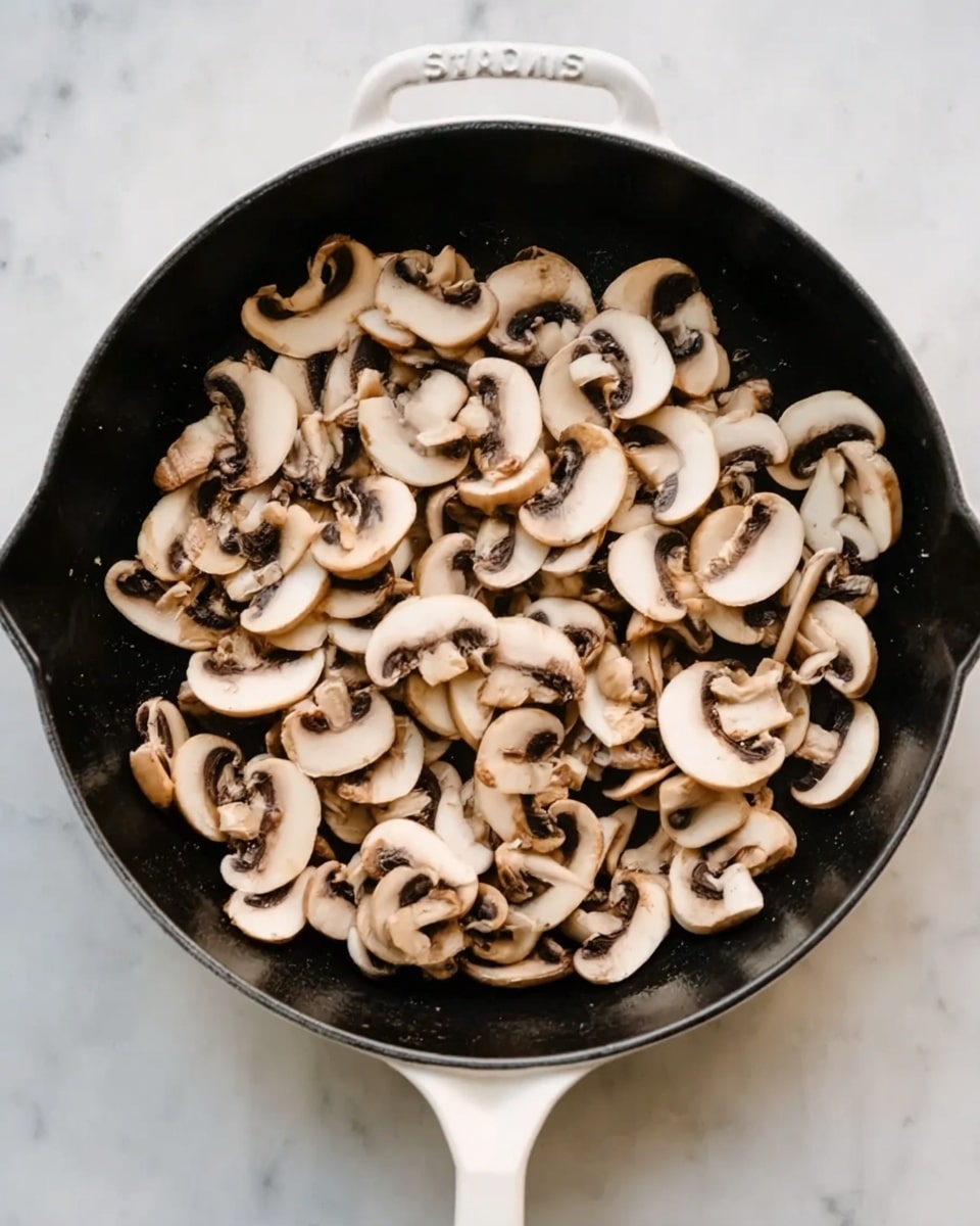A close-up view of a black cast iron pan with a white handle filled with thinly sliced raw mushrooms scattered evenly across the surface. The mushrooms are light beige with darker brown edges and have a fresh, smooth texture. The pan sits on a white marbled textured surface that gives a clean and bright background to the image. photo taken with an iphone --ar 4:5 --v 7