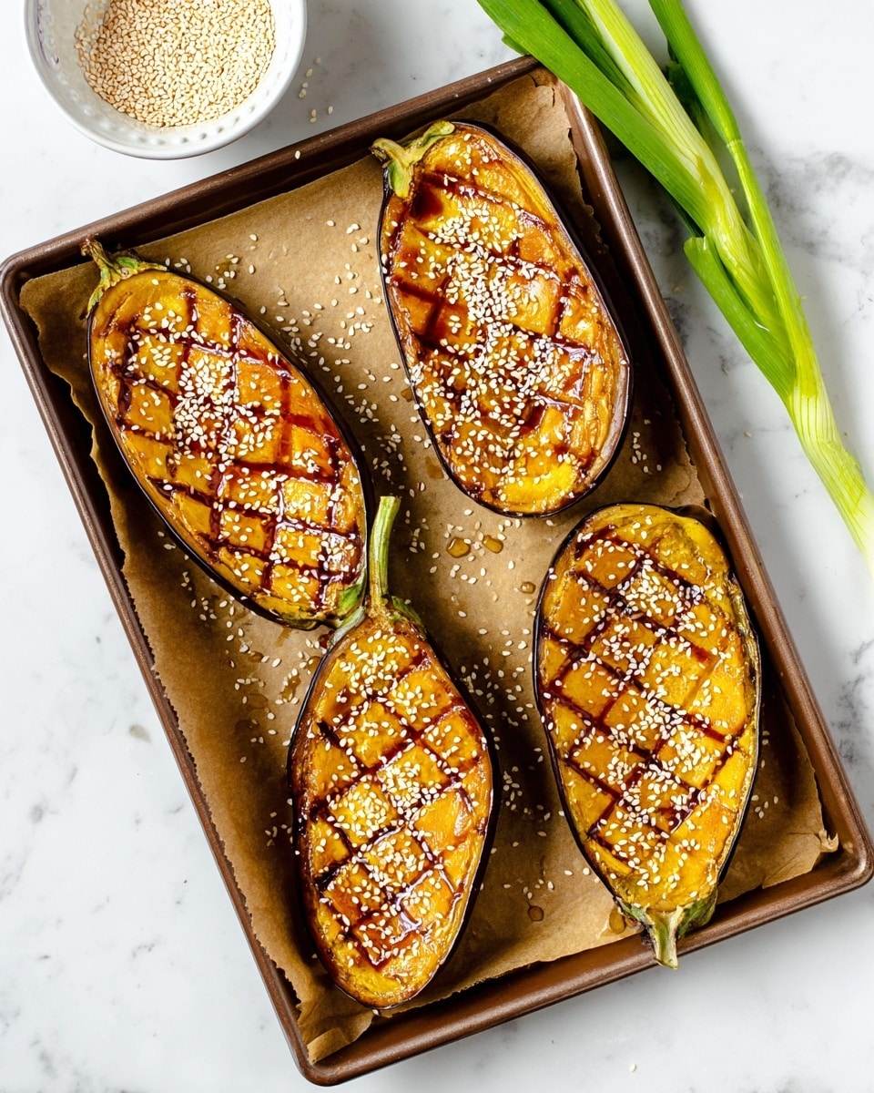 The image shows four halves of roasted eggplants on a baking tray lined with parchment paper, each eggplant half has a crisscross pattern cut into the yellow-orange flesh, covered in a shiny brown glaze and sprinkled with white sesame seeds. The tray is set on a white marbled surface with a small white bowl of sesame seeds at the top left corner and a few green onions placed on the right. Photo taken with an iphone --ar 4:5 --v 7