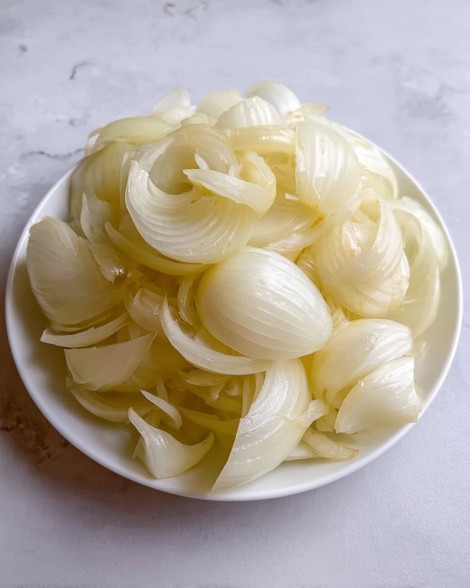 A white plate filled with a pile of pale yellow, translucent onion layers. Each onion layer is smooth and curved, some pieces are hollow and some are tightly curled, showing fine textures and slight shine on their surfaces. The onion pieces are closely stacked, creating a soft, rounded mound in the center of the white plate, which is placed on a white marbled surface. Photo taken with an iphone --ar 4:5 --v 7
