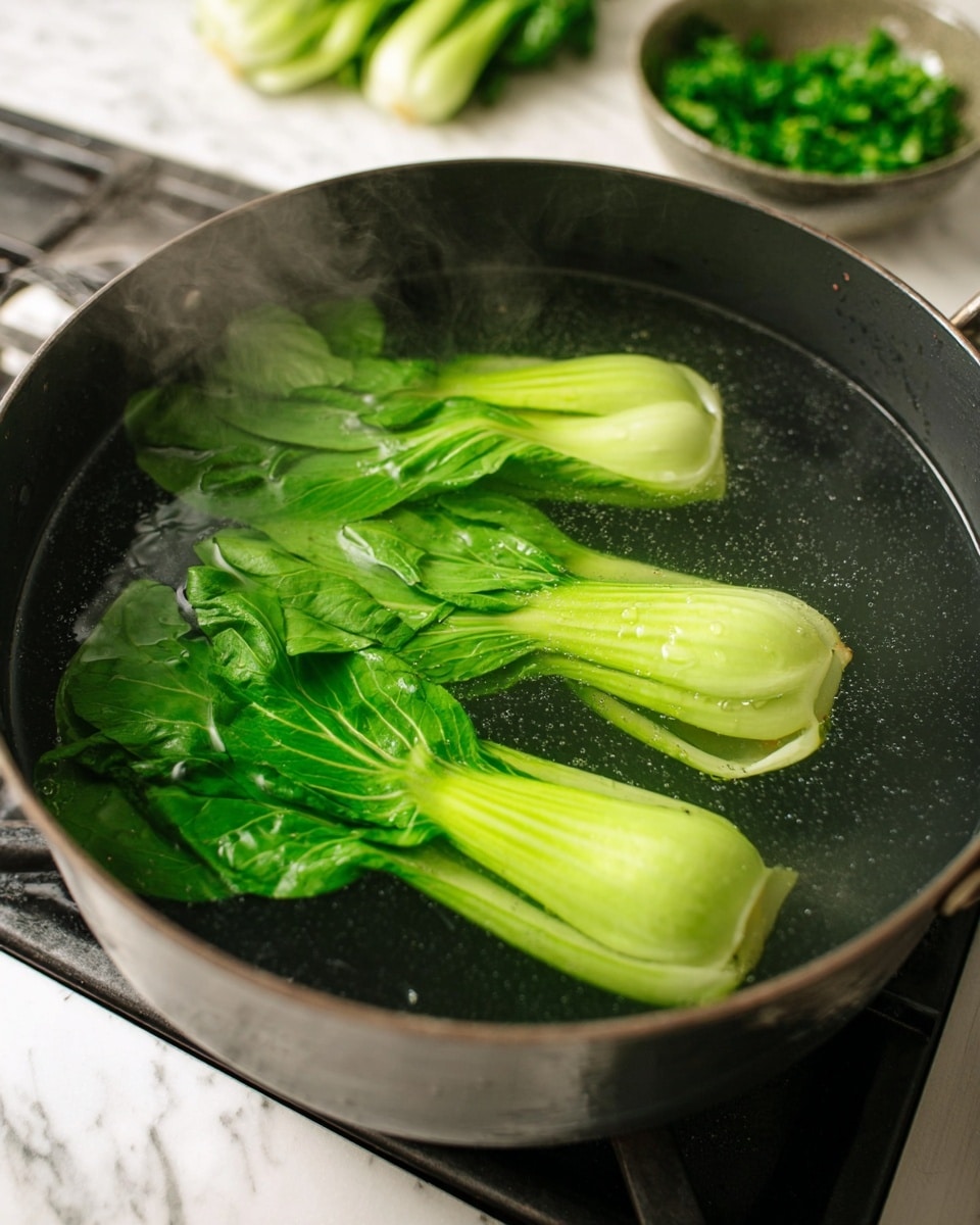 A large black pot is filled with clear boiling water, lightly steamy, inside which two whole green bok choy vegetables float. The bok choy have bright green leaves on top and pale green, almost white stalks at the base. The pot sits on a stove top with a white marbled surface visible around it. In the background, there is a blurred bowl of chopped green herbs and a bunch of more greens. The scene focuses on the fresh green vegetables and the simmering water, showing simple cooking in a home kitchen setting photo taken with an iphone --ar 4:5 --v 7
