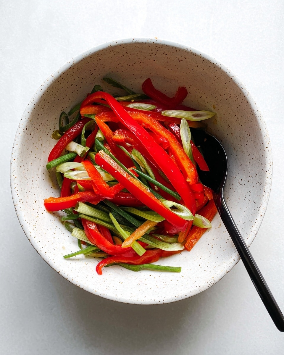 Korean Ground Beef with Spicy Red Pepper Salad Recipe 4 In a white bowl with speckles, there are long strips of red bell peppers layered with thin green onion sticks, all mixed gently with a black spoon resting inside the bowl on the right side. The vegetables look fresh with bright red and green colors, and the bowl sits on a surface with a white marbled texture. Photo taken with an iphone --ar 4:5 --v 7