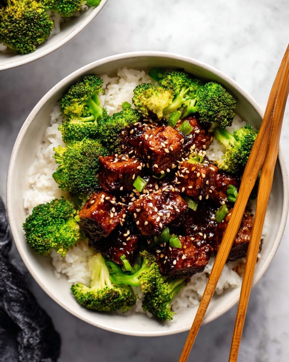 A white bowl filled with a base layer of white rice, topped with bright green broccoli florets around the edges, and a thick layer of dark brown glazed tofu cubes covered in sesame seeds sits in the center. Some chopped green vegetable pieces are mixed with the tofu. Light brown wooden chopsticks rest on the right side of the bowl. The bowl is placed on a white marbled textured surface with part of another similar bowl visible at the top left corner. photo taken with an iphone --ar 4:5 --v 7