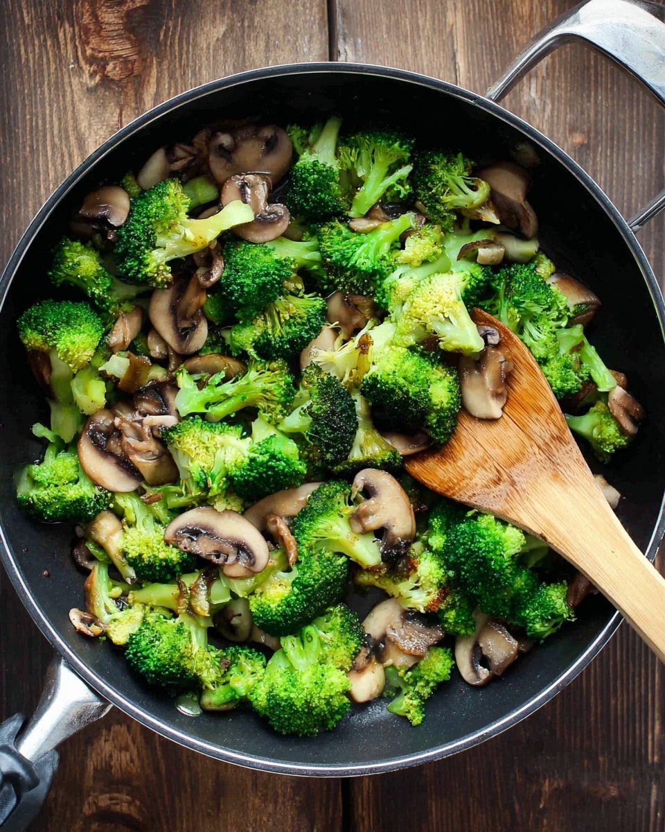 A black pan filled with cooked broccoli and sliced mushrooms on a wooden surface, the broccoli is bright green with some parts slightly yellowish, and the mushrooms are light brown and tender-looking; a wooden spatula is resting in the pan touching the vegetables, showing texture and freshness. photo taken with an iphone --ar 4:5 --v 7