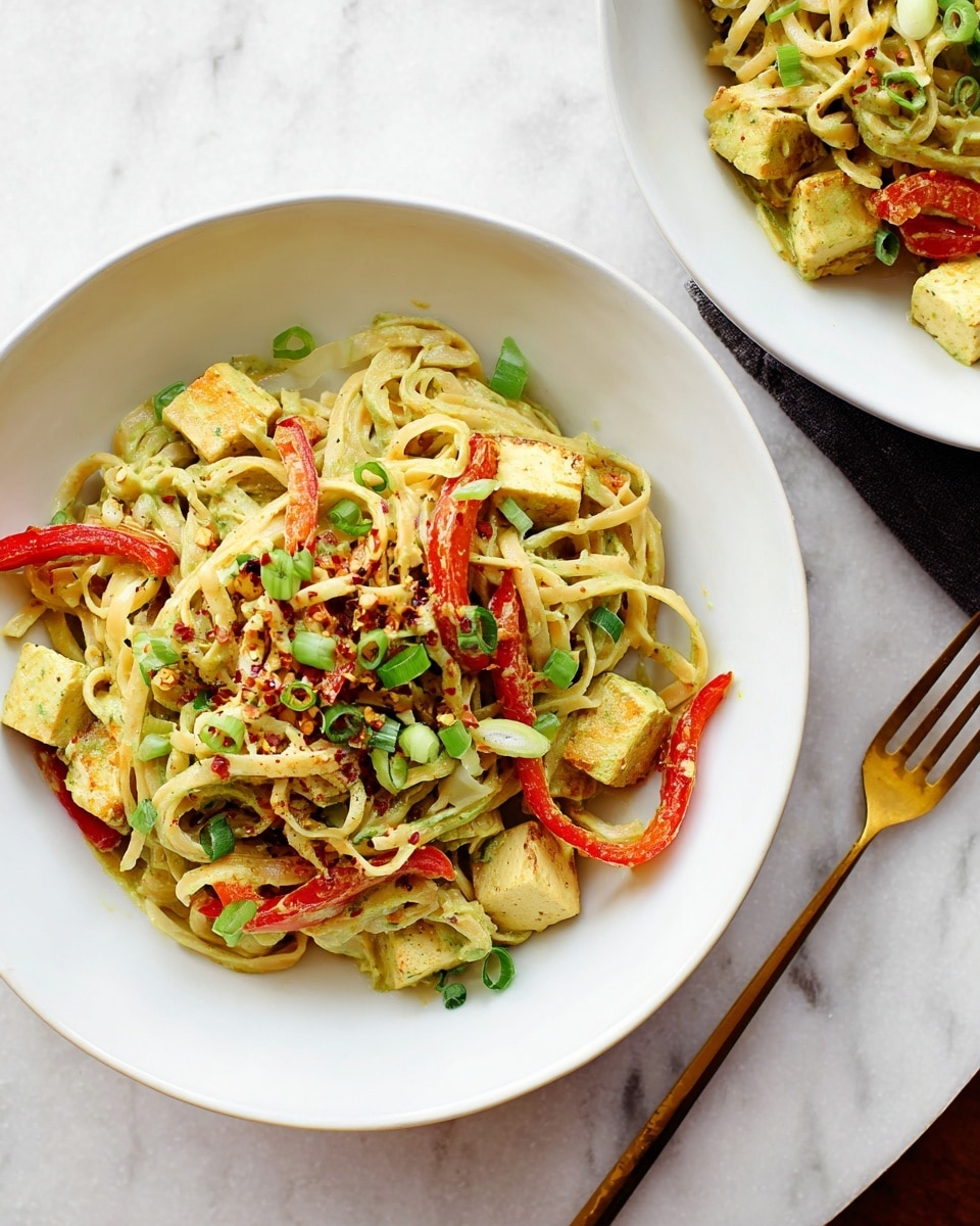 A white bowl filled with a dish made of several layers: the base layer shows pale yellow noodles mixed with light green curry sauce coating them unevenly, scattered with small, light yellow tofu cubes throughout. Thin slices of bright red bell pepper are spread across the noodles, adding contrast, while finely chopped green onions are sprinkled on top. A small amount of red chili flakes adds speckled red dots over the dish. The bowl sits on a white marbled surface, with a golden fork placed to the right. Part of another white bowl with the same dish is visible at the top right corner. photo taken with an iphone --ar 4:5 --v 7