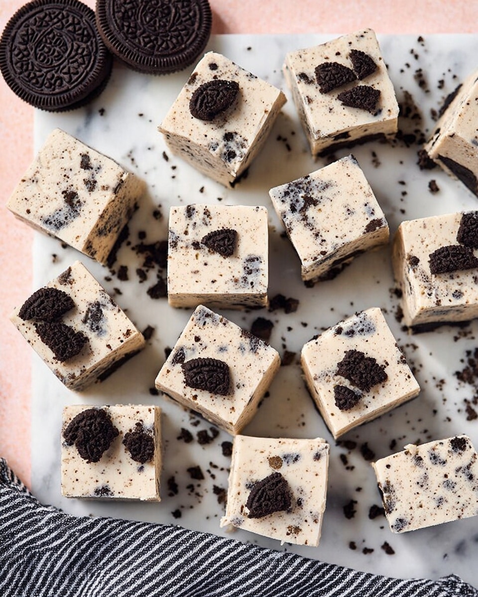 The image shows fifteen square pieces of cookies and cream fudge arranged on a white marbled surface with some pieces slightly overlapping each other and some tilted to show their thickness. Each fudge piece has a creamy light beige base with specks of crushed dark chocolate cookies evenly mixed throughout, and some topped with partial cookie halves or cookie crumbs. In the top left corner, two whole dark chocolate sandwich cookies rest with some scattered cookie crumbs nearby. A black and white striped cloth is partly visible at the bottom edge of the photo. photo taken with an iphone --ar 4:5 --v 7
