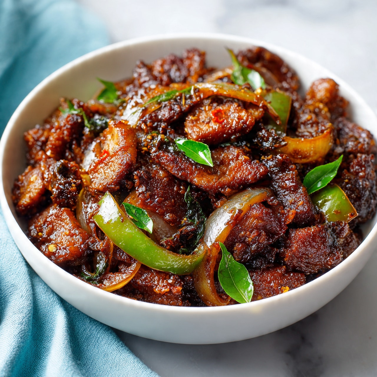 A close-up view of a white bowl filled with dark brown cooked pieces of textured meat mixed with translucent caramelized onion slices and small green bell pepper pieces, all coated with a rich, thick sauce. Small bright green herb leaves are scattered on top, adding contrast. The bowl is placed on a white marbled surface with a soft blue cloth slightly visible in the corner. The dish looks hearty and savory, with a mix of rough and smooth textures on the meat and vegetables photo taken with an iphone --ar 4:5 --v 7