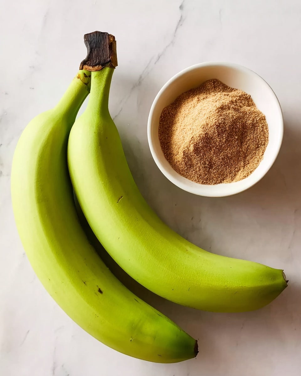 Two whole green bananas with dark tips lie side by side on a white marbled surface. Next to them is a small white bowl filled with a mix of light brown and darker brown powders, likely spices or sugar, with a slightly rough texture visible on the powders. The arrangement is simple and clean, with soft natural light illuminating the items. photo taken with an iphone --ar 4:5 --v 7