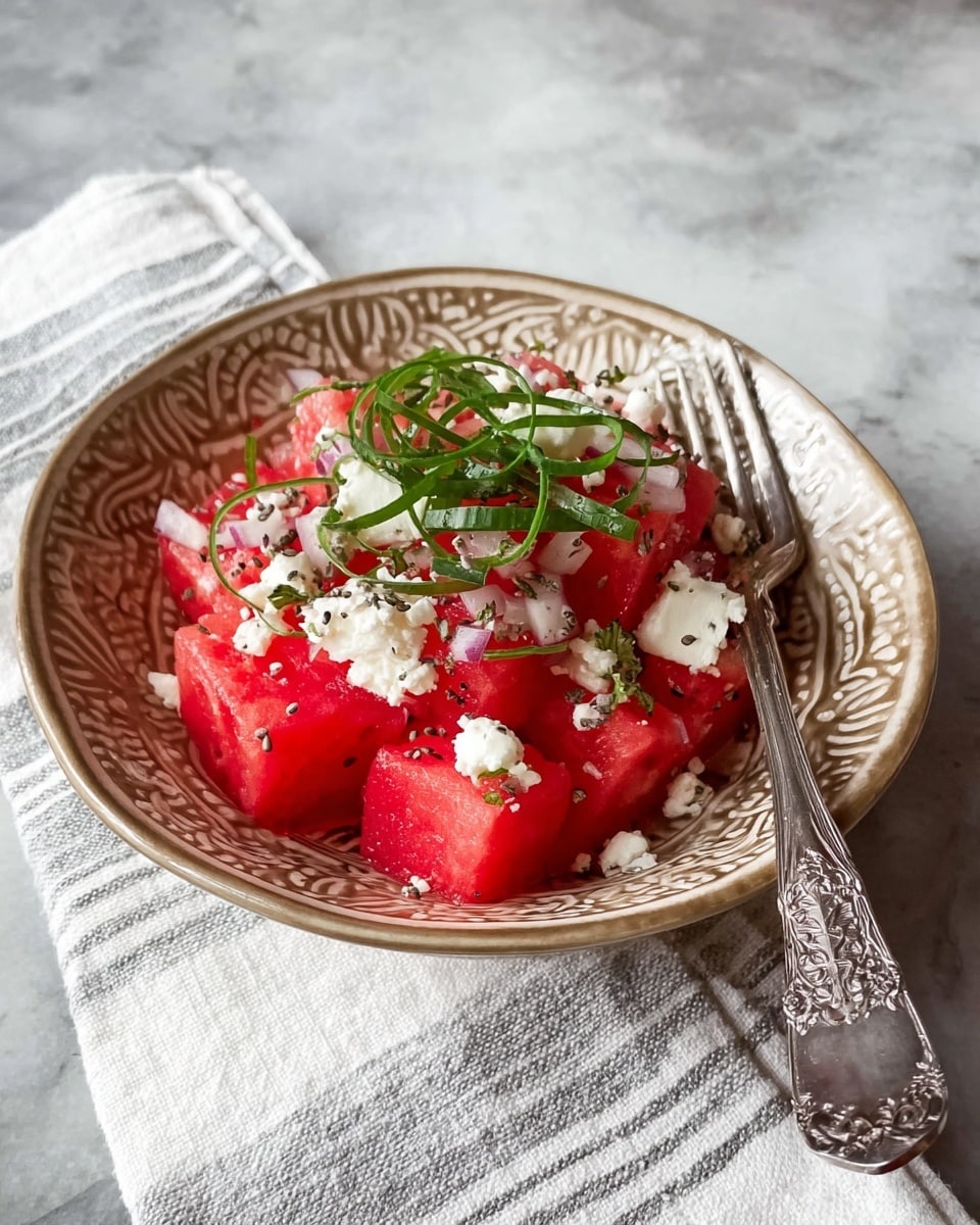A decorative beige bowl with ornate patterns holds a salad made of bright red watermelon cubes layered on the bottom. On top of the watermelon are small white chunks, likely cheese, sprinkled with black seeds and finely chopped red onions. The salad is garnished with thin green curled strips, placed neatly on the top center. A silver fork with an intricate design rests on the right side of the bowl. The bowl sits on a white cloth with light gray stripes, all placed on a white marbled surface. Photo taken with an iphone --ar 4:5 --v 7