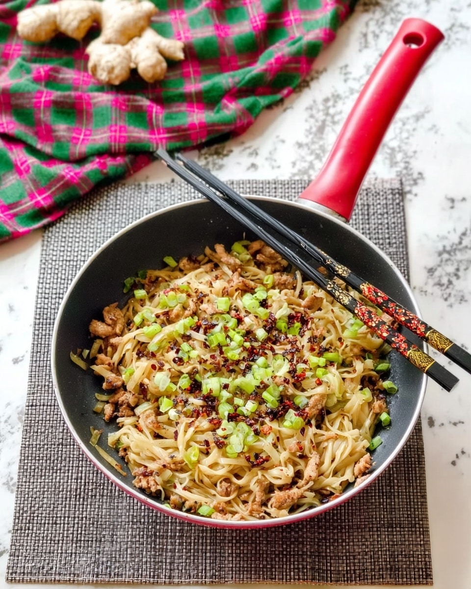 A frying pan with a red handle sits on a gray woven mat on a white marbled surface. Inside the pan, there are three layers visible: the bottom layer is cooked, light brown noodles mixed with bits of meat, the middle layer has small chopped green onions sprinkled evenly, and on top, there are tiny black and red spices scattered around. Two black chopsticks with gold and red designs lie across the pan's top edge. In the background, a green and pink plaid cloth is spread out with pieces of ginger and garlic placed on top. Photo taken with an iphone --ar 4:5 --v 7