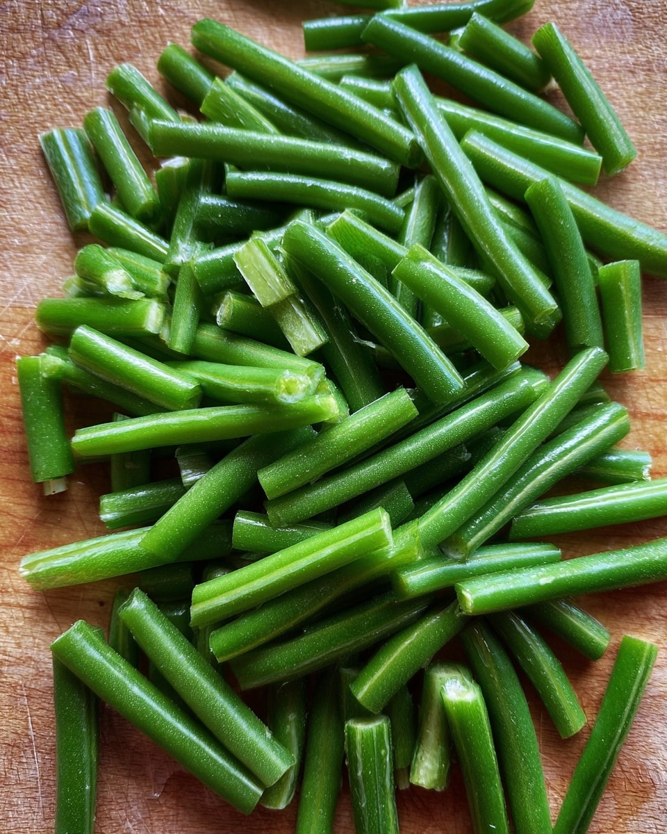 The image shows many short green beans chopped into small pieces, each piece bright green and smooth, lying loose on a wooden surface. The beans are fresh and vibrant, with a slight shine on their skin, packed closely but spread out in an even layer. The background is not detailed in the description but is a wooden texture under the beans. Photo taken with an iphone --ar 4:5 --v 7