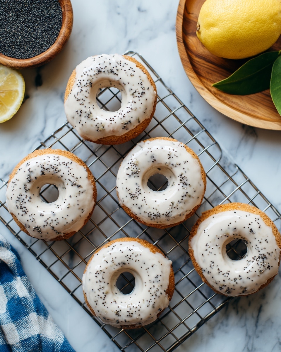 Five light beige donuts with white icing and small black poppy seeds sprinkled over on top are placed on a silver metal cooling rack set on a white marbled surface. In the top left corner, there is a wooden bowl filled with black poppy seeds and next to it, a wooden plate holds a half lemon with green leaves. A blue and white checkered cloth is visible in the bottom left corner. Photo taken with an iphone --ar 4:5 --v 7