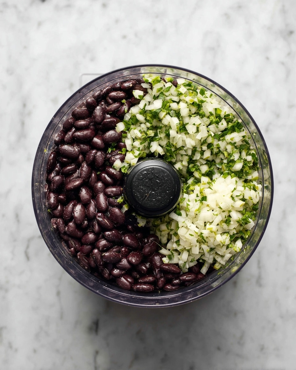 A clear food processor bowl viewed from above contains two main layers. The lower layer fills about two-thirds of the bowl and is made of dark purple-black beans with a shiny, wet texture. On top of these beans, there is a finely chopped layer of white and light green vegetables, likely onions and jalapeños, occupying about one-third of the bowl. The bowl sits on a white marbled surface, and the black central column of the processor is clearly visible in the middle. photo taken with an iphone --ar 4:5 --v 7