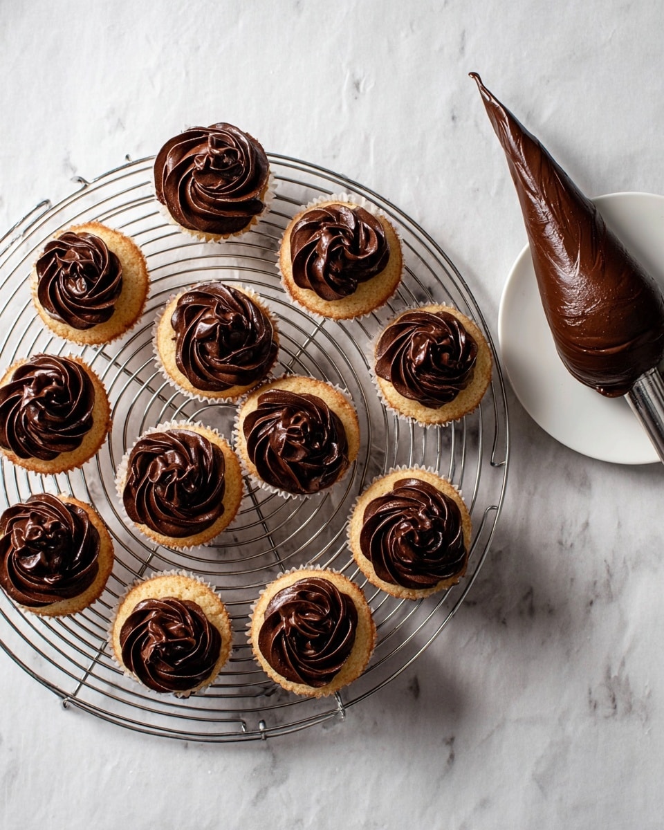 There are twelve cupcakes on a round metal cooling rack with an open spiral design, each cupcake has one layer of light brown cake topped with one thick layer of dark brown, smooth chocolate frosting swirled in a flower shape. The rack is placed on a white marbled surface. To the right side of the image, a white small round plate holds the tip of a piping bag filled with glossy dark brown chocolate frosting, the rest of the piping bag lies next to the plate. The photo taken with an iphone --ar 4:5 --v 7