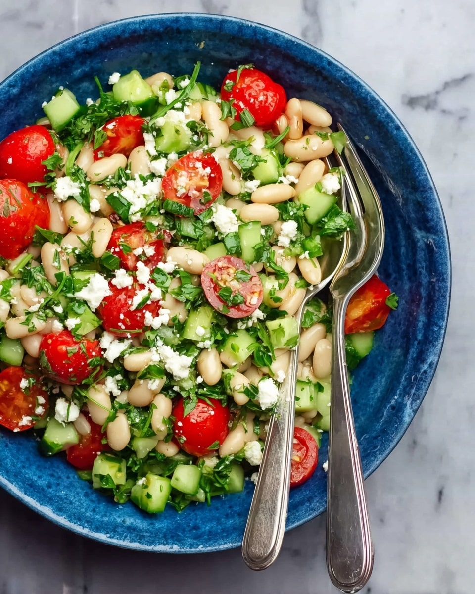 A blue bowl filled with a fresh salad consisting of white beans scattered throughout, halved bright red cherry tomatoes, and chopped green cucumber pieces. The salad is garnished with crumbled white cheese and finely chopped green herbs like parsley and arugula. Two silver forks rest side by side on the right edge of the bowl. The bowl is placed on a white marbled surface photo taken with an iphone --ar 4:5 --v 7
