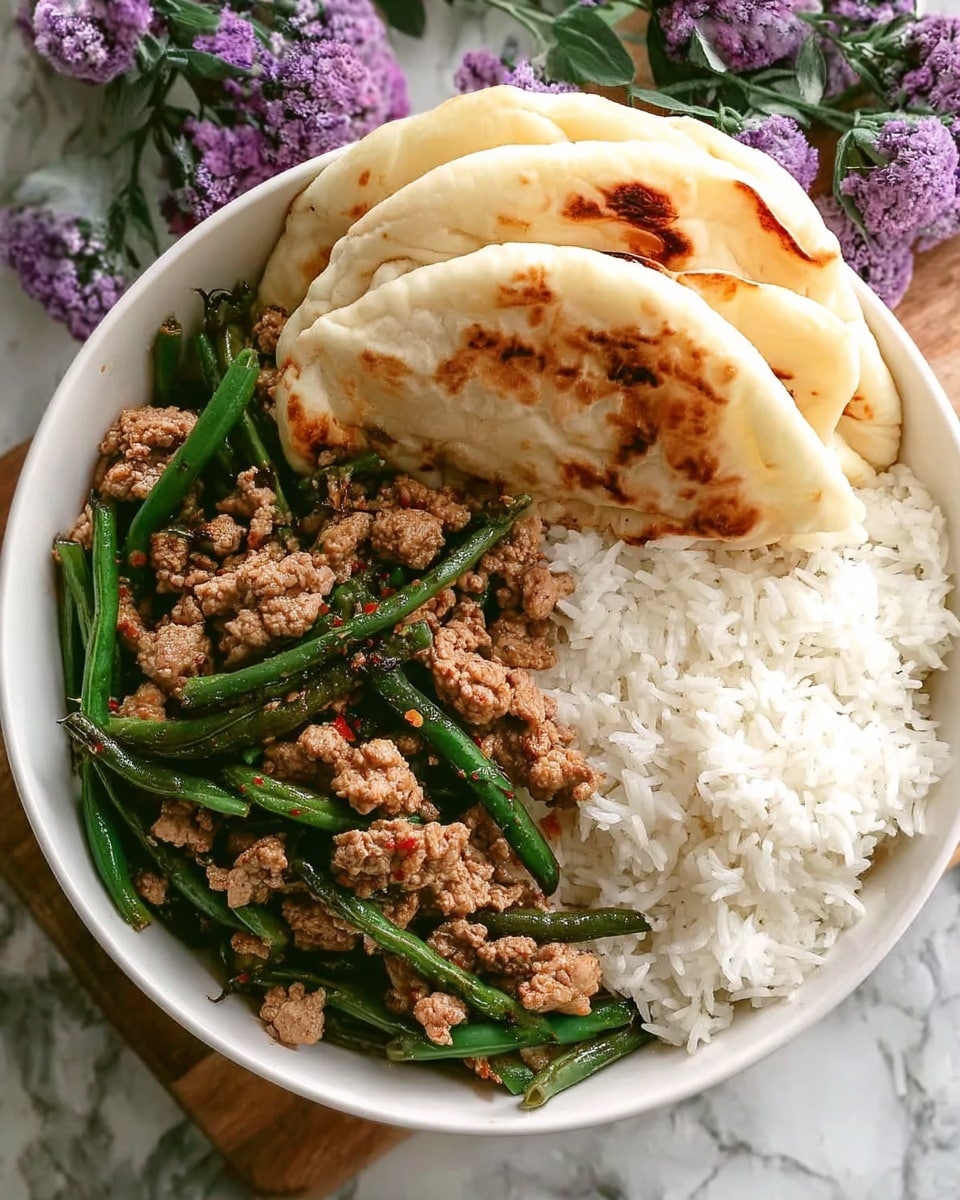 This image shows a white bowl filled with three main layers: on the left, there is a mix of cooked ground meat and green beans, with the meat pieces small and brownish, and the beans long and green, layered evenly together. On the right side, there is a fluffy bed of white rice with a soft texture. At the top of the bowl, resting partly on the rice, are two pieces of flatbread that are light tan with some brown spots showing where they are toasted. The bowl is placed on a white marbled surface with some purple flowers in the background. Photo taken with an iphone --ar 4:5 --v 7