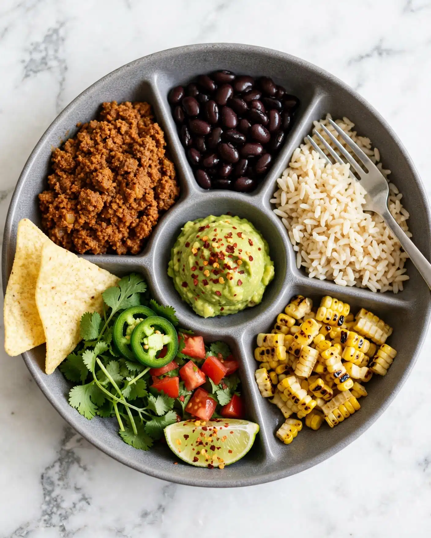 A close-up view shows a wooden spoon holding a mix of cooked minced textured protein in a rich orange-brown color with bits of red and green herbs. The background displays a black pan filled with more of this cooked mix, garnished with fresh green cilantro leaves, sliced green jalapeños, and wedges of pale yellow lime arranged on one side. The scene is set on a white marbled surface with a few cilantro leaves scattered around. The lighting highlights the texture and brightness of the food, and a woman's hand holds the wooden spoon in focus. photo taken with an iphone --ar 4:5 --v 7