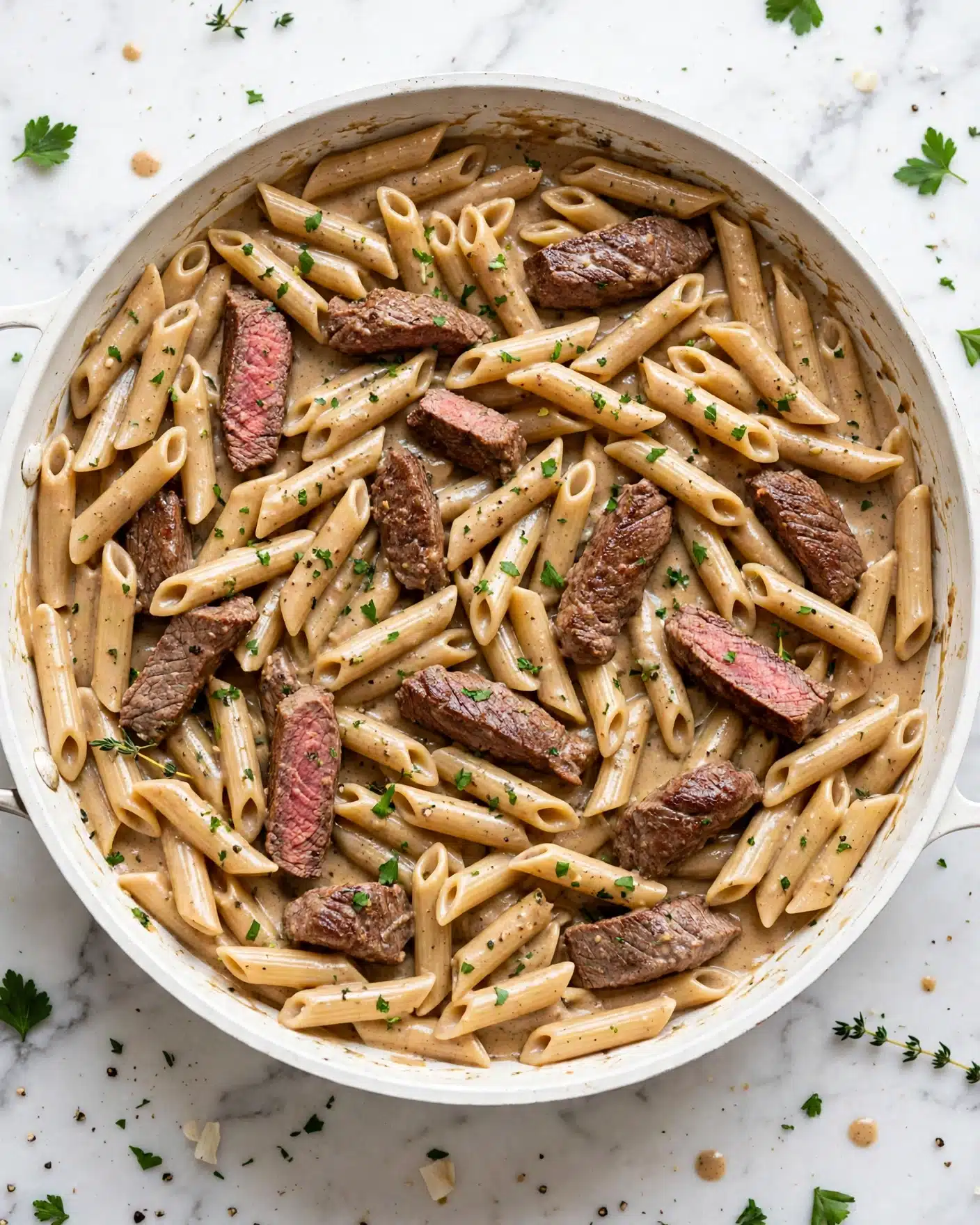 The image shows a white pan filled with creamy pasta mixed with pieces of cooked meat. The pasta is light beige and tube-shaped, coated in a smooth, light brown sauce. Scattered throughout the pasta are medium-sized pieces of browned meat with a slightly pink center. On top, there are small green herb leaves sprinkled evenly, adding a fresh touch. The pan sits on a white marbled surface creating a clean background. Photo taken with an iphone --ar 4:5 --v 7